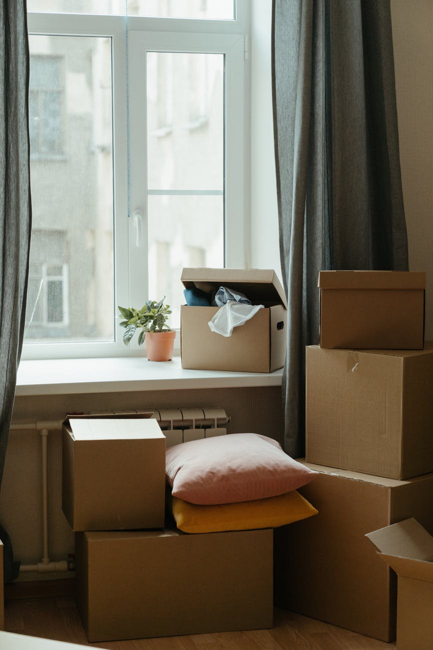 Packed boxes and pillows stacked near a window.